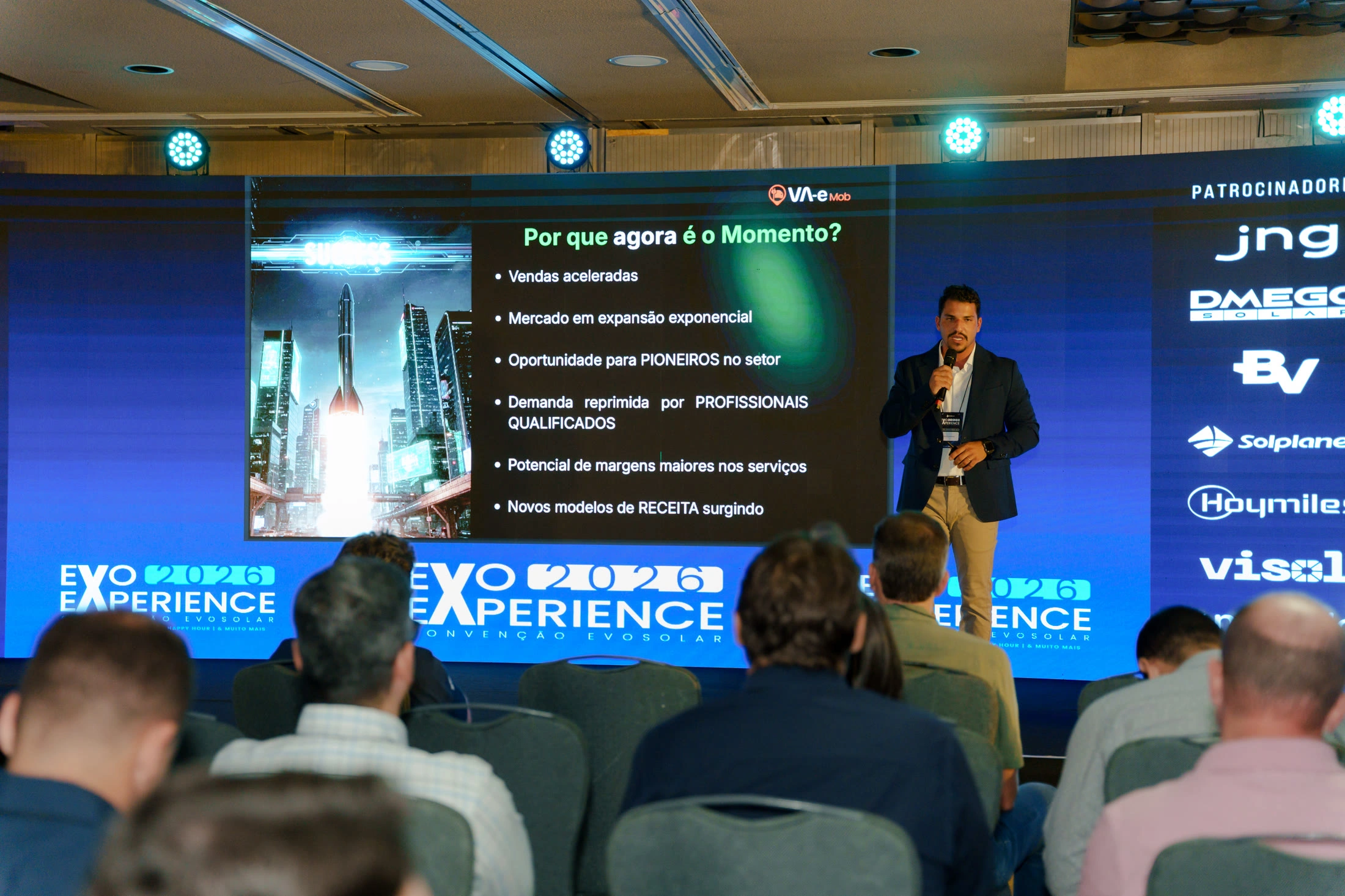 Nickollas Gobira no palco da convenção de 2026, diante do slide “Por que agora é o momento?”
